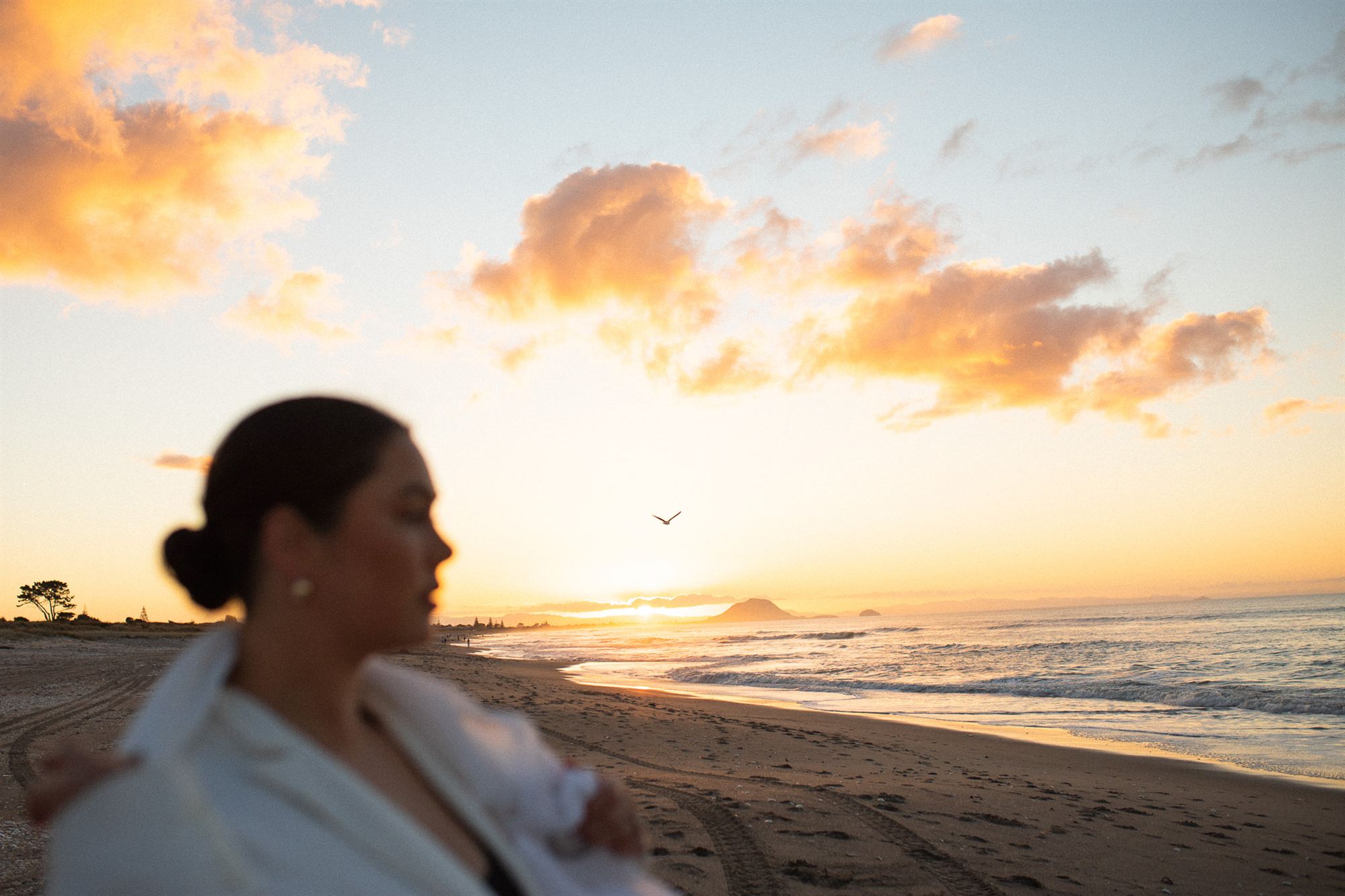A woman on the beach at sunrise, the sun breaking over the headland